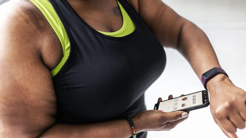 A woman wearing athletic outfit checks her fitness data on her smartphone