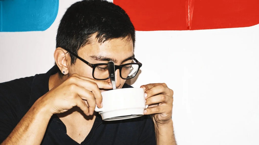 A man wearing glasses sips on a bowl of soup