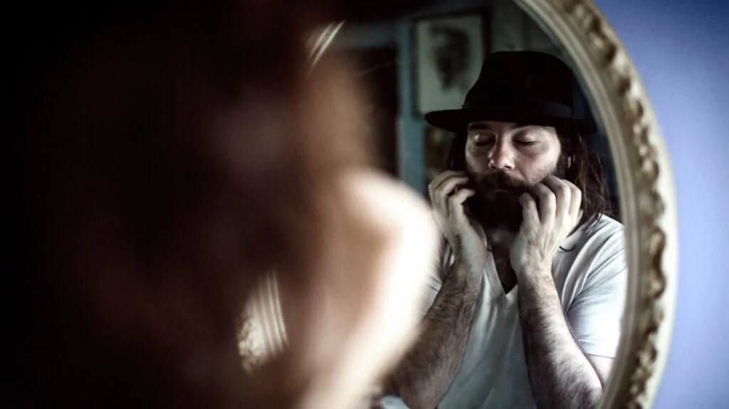 A man looks in a mirror while scratching his beard