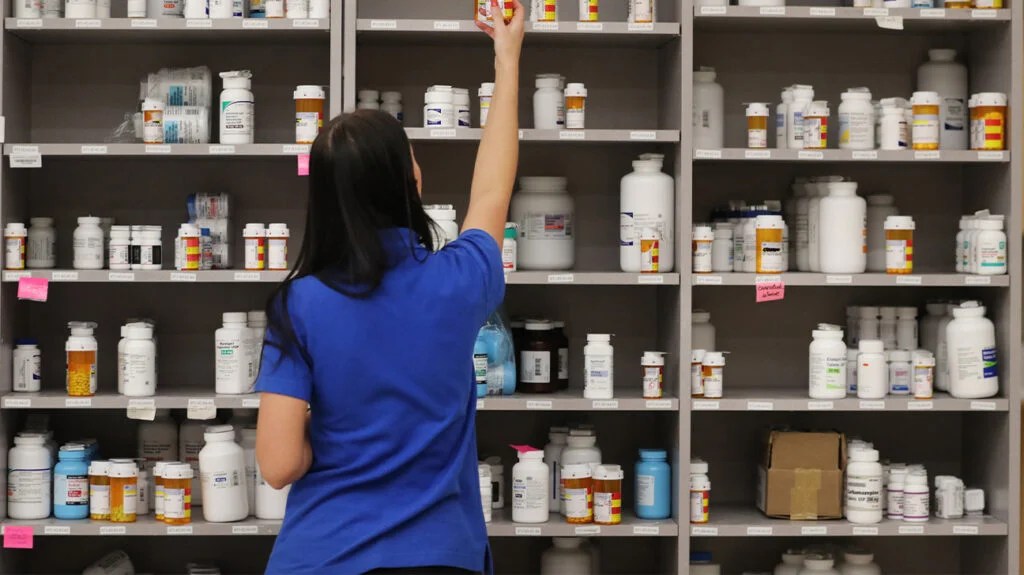 pharmacist reaching for a drug on a shelf